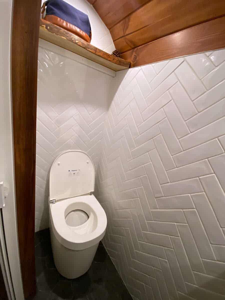 Composting toilet in a white herringbone-tiled room with a wood-plank ceiling