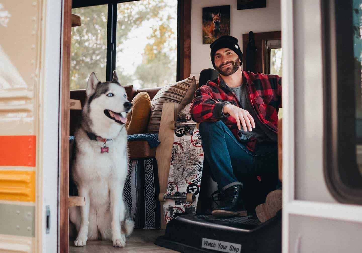 Jonathan Perera sitting in the driver's area of his converted bus with his Siberian Husky, Skye