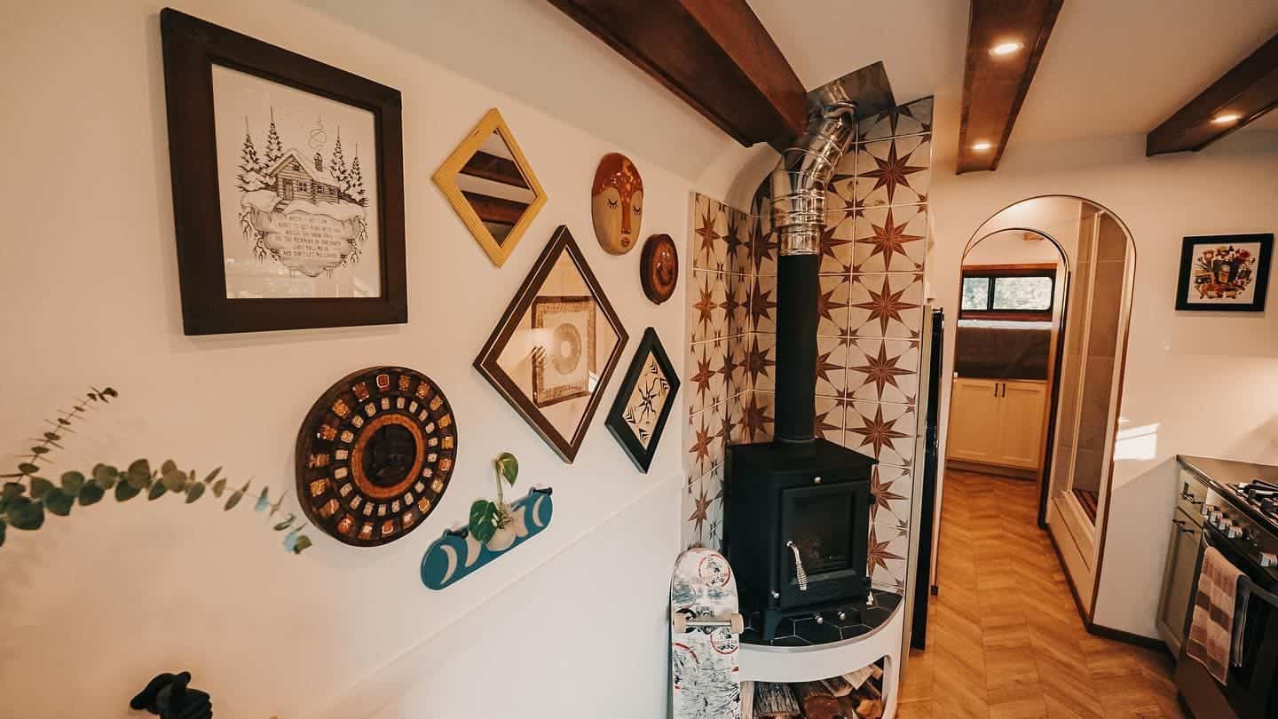 Gallery wall of art and mirrors beside the wood stove, with an arched hallway leading toward the bedroom