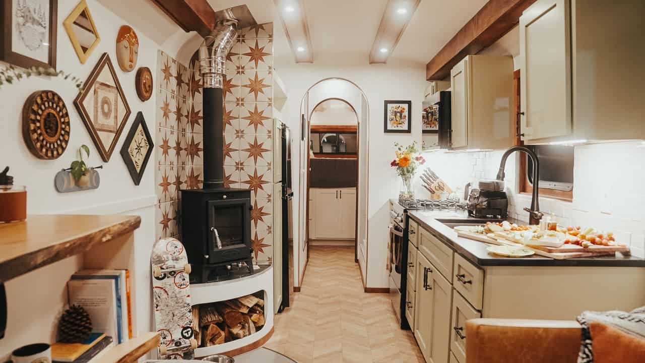 Galley kitchen with sage-green cabinets, black countertops, a brick backsplash, and a wood stove with star-pattern tile
