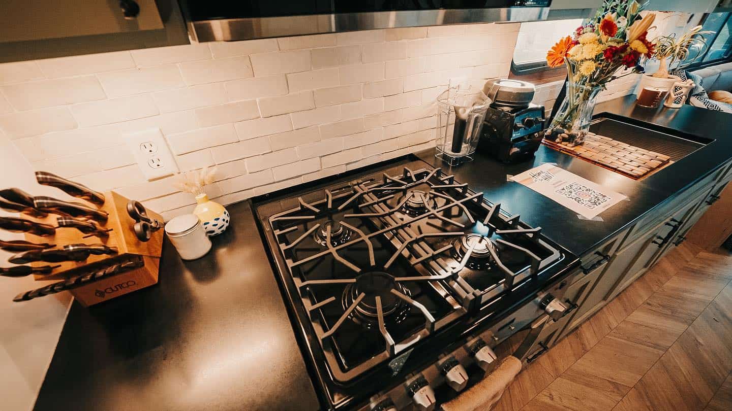 Full-size four-burner propane gas range set into a black countertop with a brick backsplash