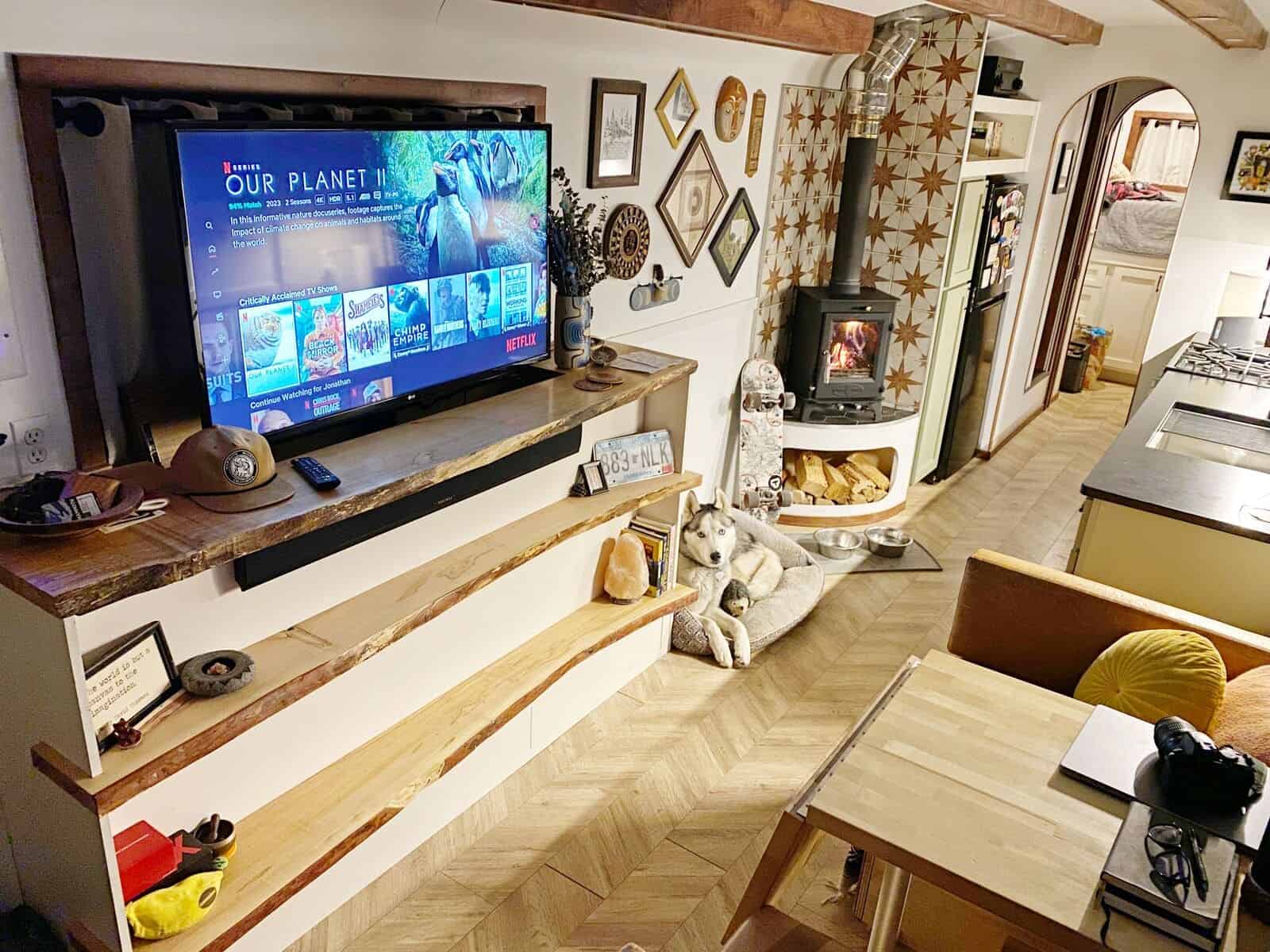 Living area with a hidden TV in ambrosia-maple shelving and a wood stove on a curved tiled hearth
