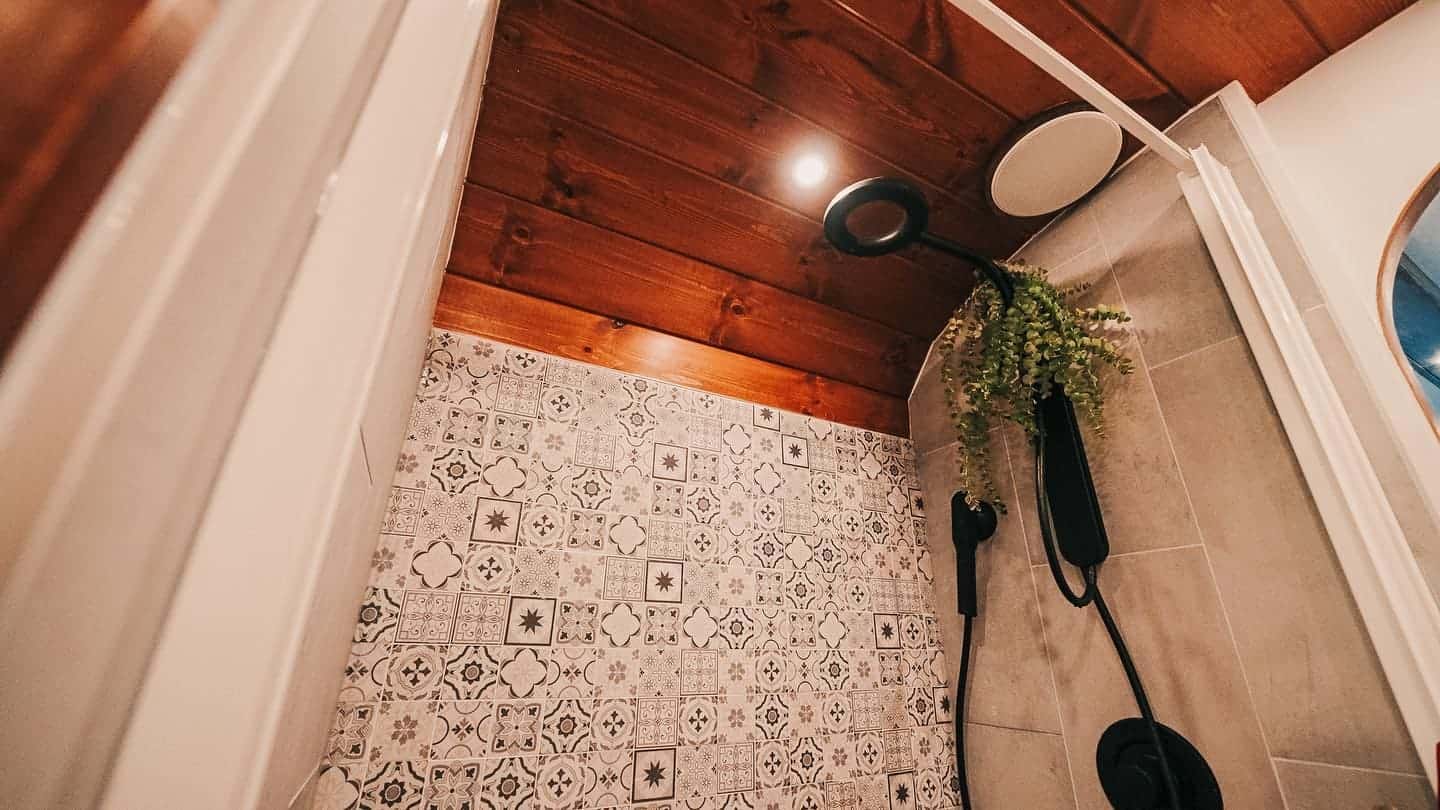 Tiled shower with a teak ceiling, Nebia spa shower head, hanging plant, and a built-in speaker