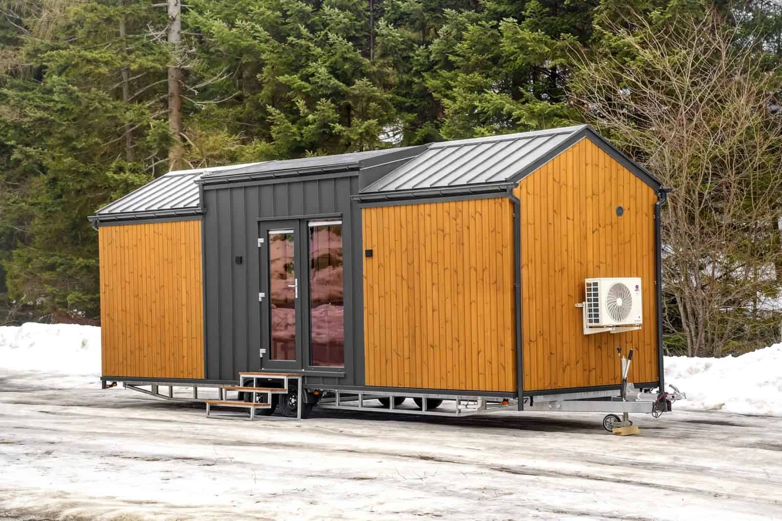 Exterior of the Justine tiny house with wood cladding, a dark metal gable, and an air-conditioning unit