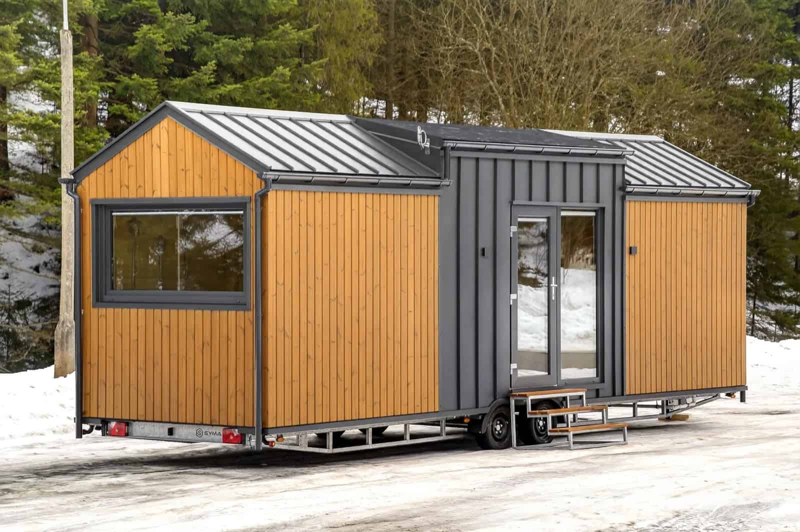 Angled exterior view of the Justine showing its long gable profile, entry door, and tandem-axle trailer