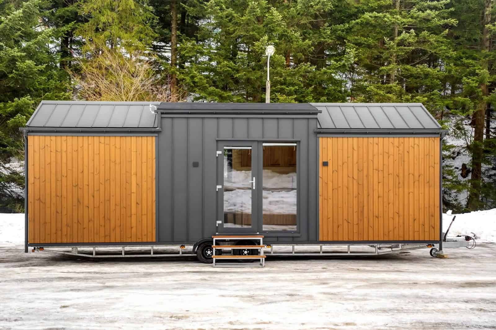 The Justine tiny house by Craft House with thermo-pine siding and a charcoal standing-seam gable roof in a snowy forest