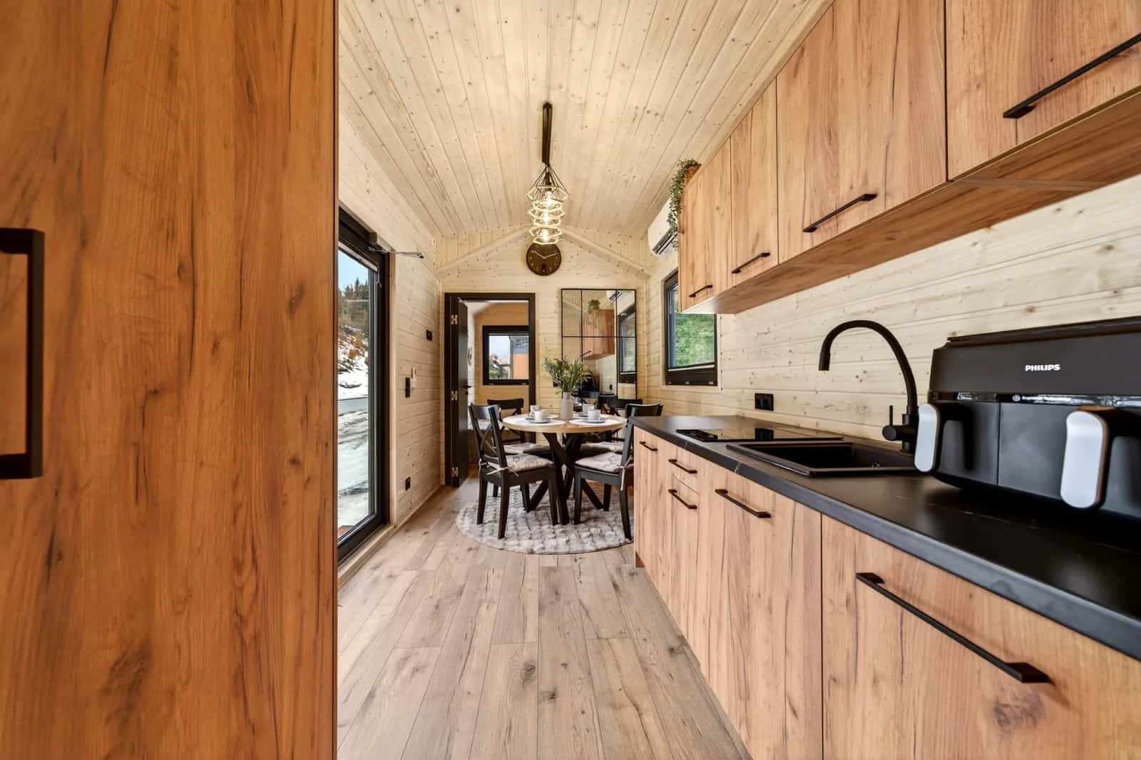 Galley kitchen in the Justine with black countertops, wood cabinetry, and a dining table by the glass door