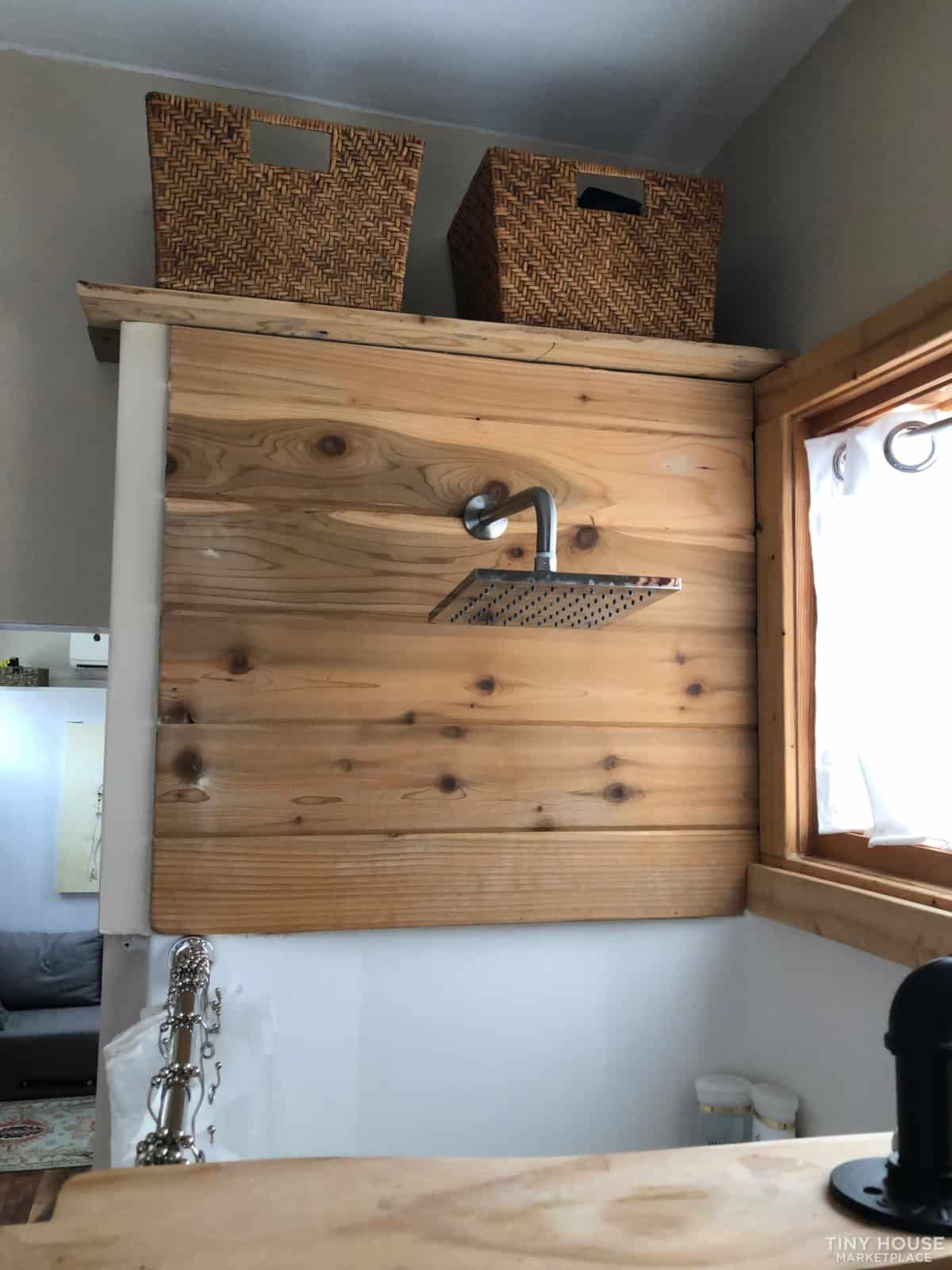 Walk-in shower with cedar wood accent wall, rain showerhead, and woven storage baskets in the Kangaroo tiny house