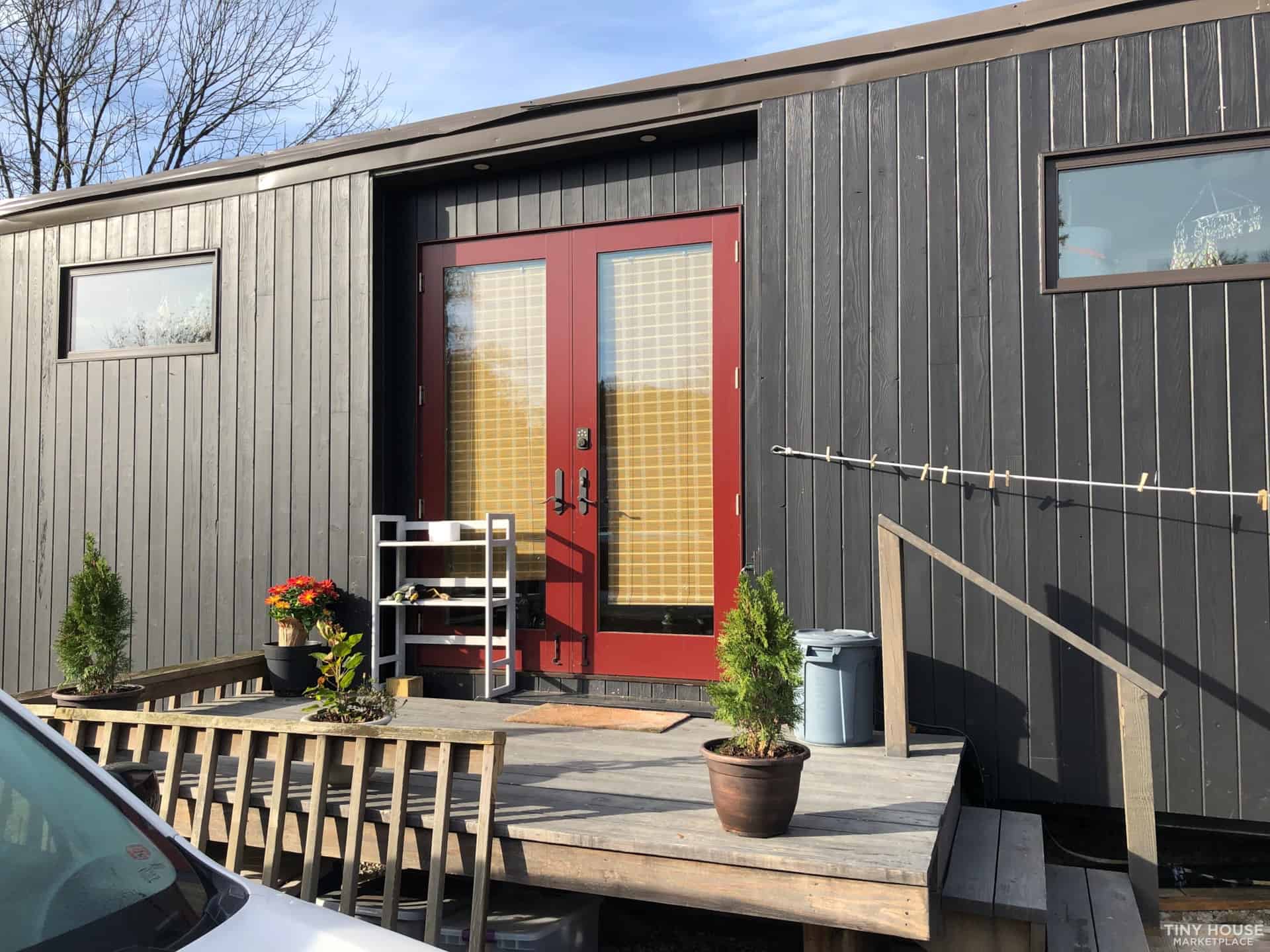 Tiny house exterior with a red door, potted plants, and outdoor seating area.