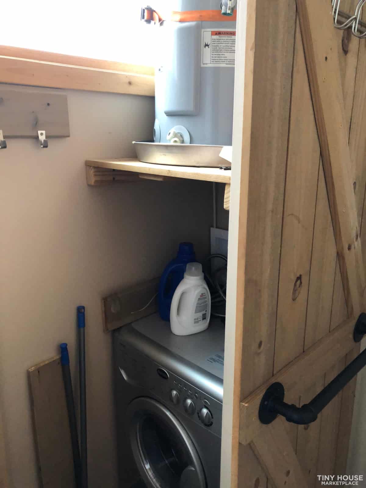 Washer-dryer combo unit tucked behind the sliding barn door with water heater mounted above in the Kangaroo THOW