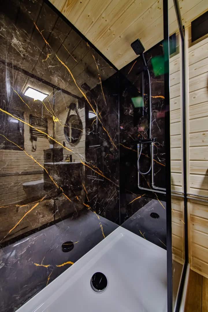 Bathroom in the Katrin with black-and-gold marble panels, a bathtub, and a glass shower