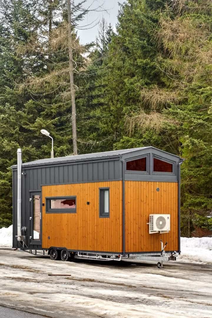 Angled exterior of the Katrin with wood cladding, a dark gable, an air-conditioning unit, and a wood-stove flue