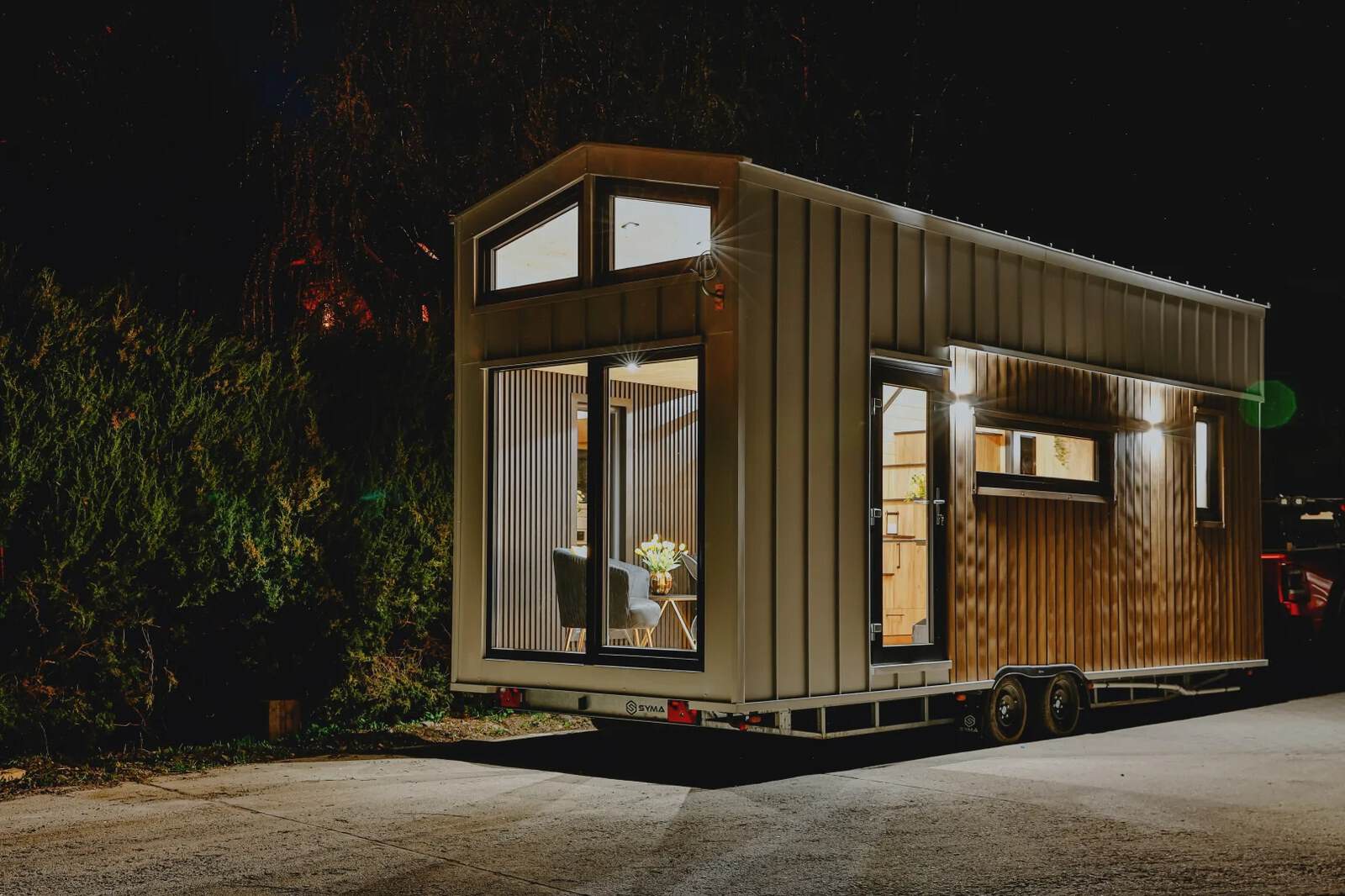 The Katrin tiny house glowing at night, shown in a lighter standing-seam finish