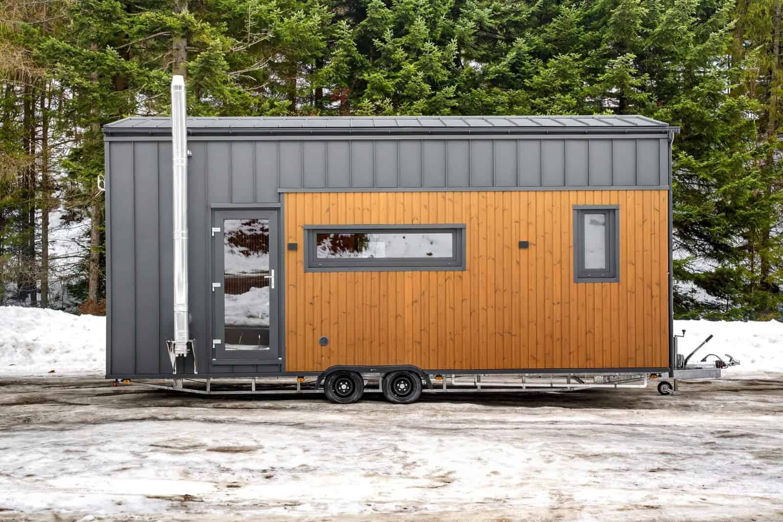 Side view of the Katrin tiny house showing the gable profile, clerestory windows, a chimney flue, and the tandem-axle trailer