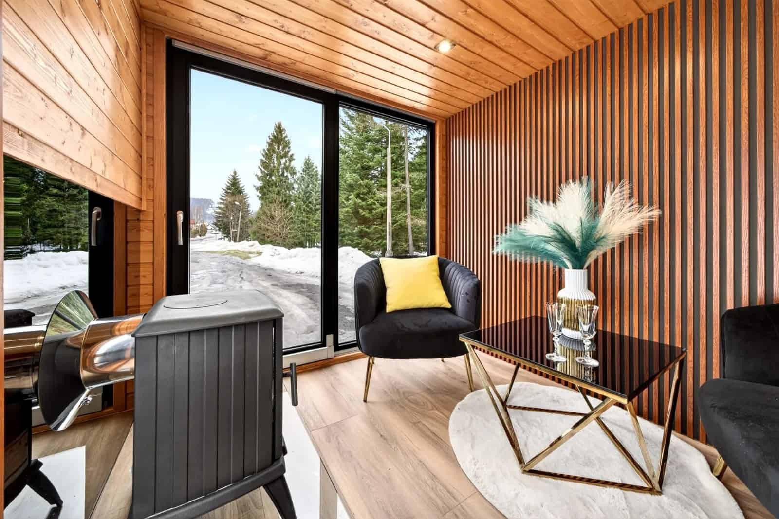 Living area of the Katrin with a wood-burning stove, a slatted wood wall, black velvet seating, and floor-to-ceiling glass