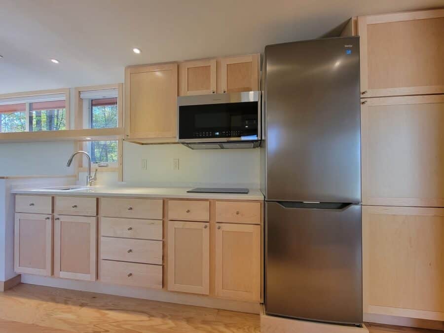 Modern tiny house kitchen with light wood cabinets and stainless steel appliances.