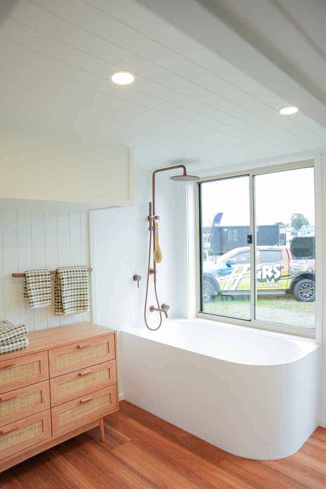 Freestanding bathtub under a window with a copper rain shower above it in the Kookaburra 2.0