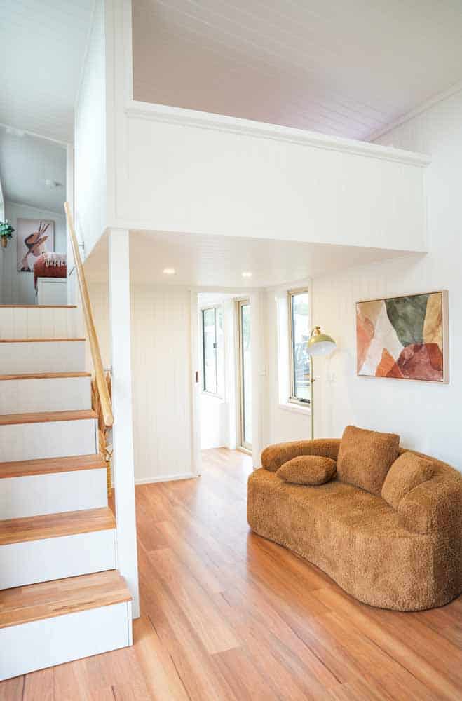 Living room in the Kookaburra 2.0 with a curved sofa, timber floors, and the loft overhang above