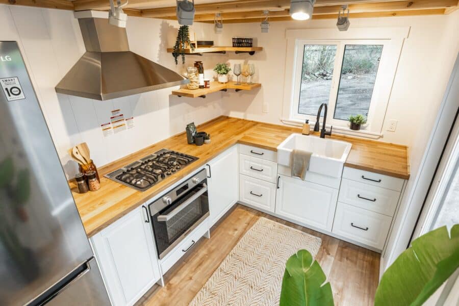 Modern tiny house kitchen with white cabinets, wooden countertops, and stainless steel appliances.