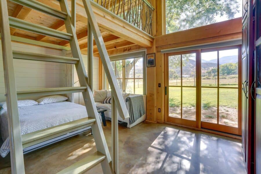 Cozy tiny house interior featuring a loft bed, large windows, and natural wood accents.