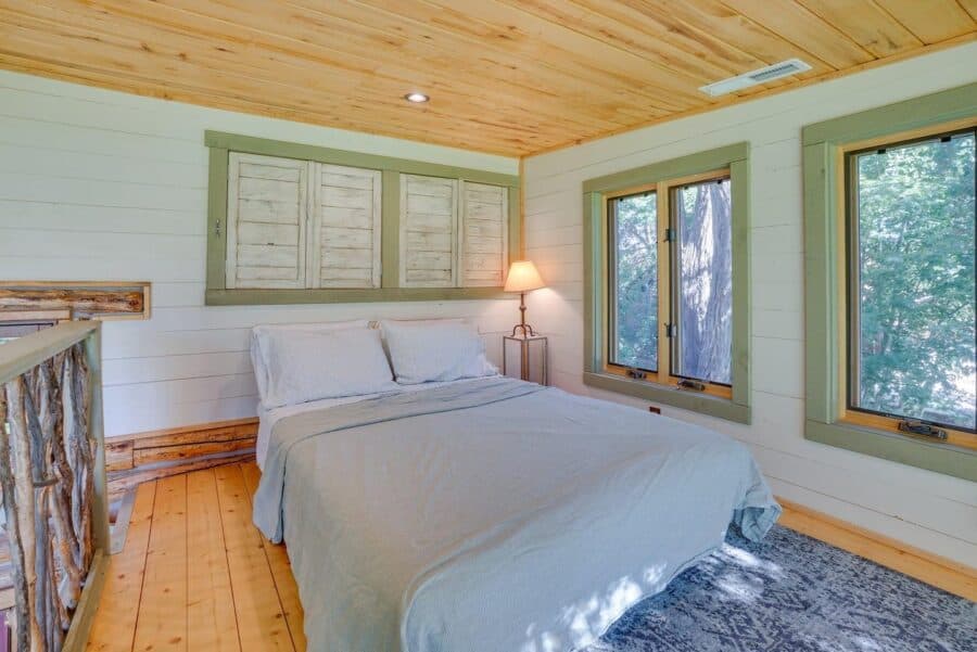 Charming log cabin bedroom featuring rustic stone accents, large windows, and natural wood finishes.