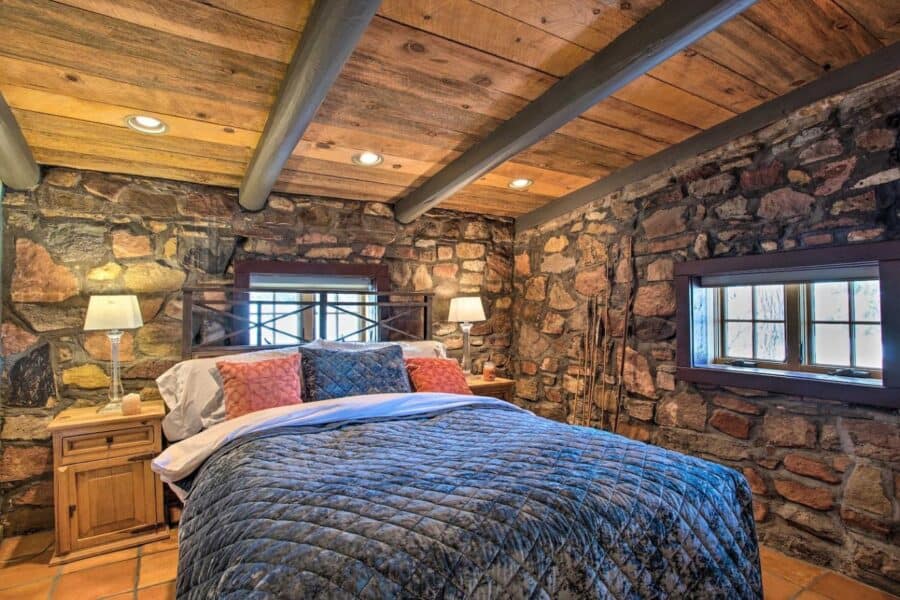 Rustic log cabin bedroom featuring stone walls and wooden ceiling beams.