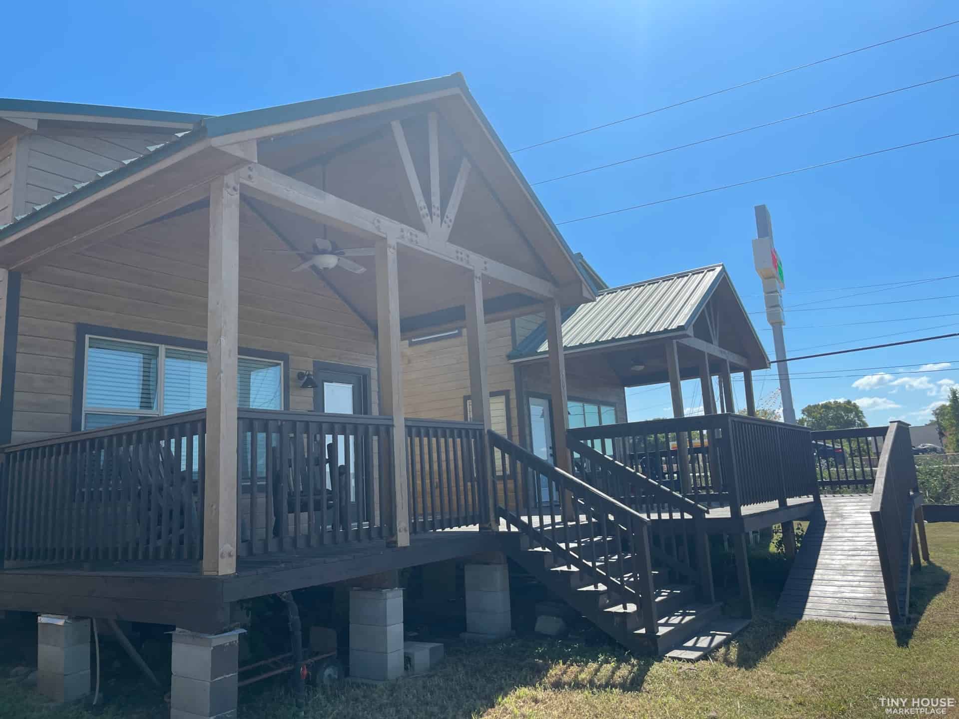Porch and ramp leading to a cozy tiny house under a bright blue sky.