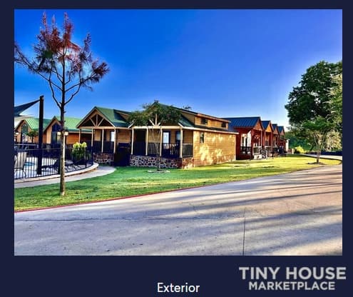 Small community of tiny houses with green lawns and trees under a clear blue sky.