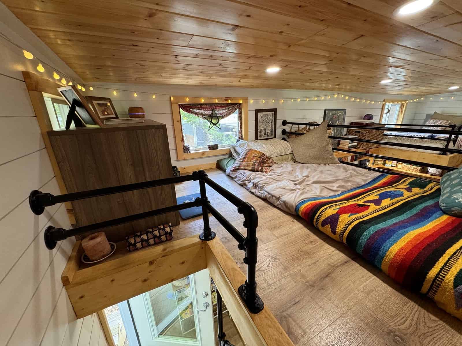 Both sleeping lofts in the Leela tiny house seen from the master loft, separated by an open stairwell with pipe railings