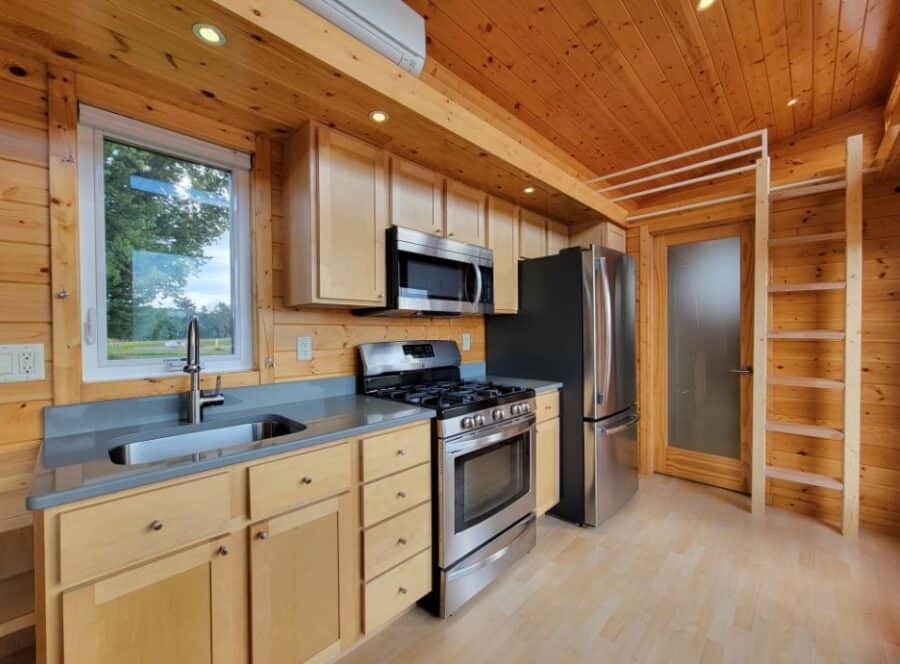 Modern tiny house kitchen with wood accents and stainless steel appliances.