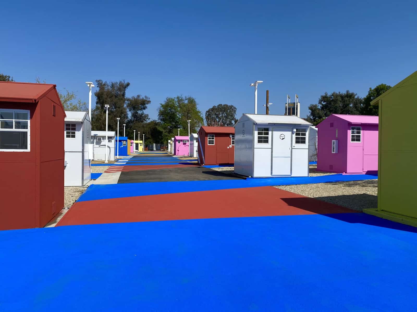 Brightly painted red, pink, white and green Pallet tiny homes lining colorful painted pathways at a Hope the Mission tiny home village in Los Angeles