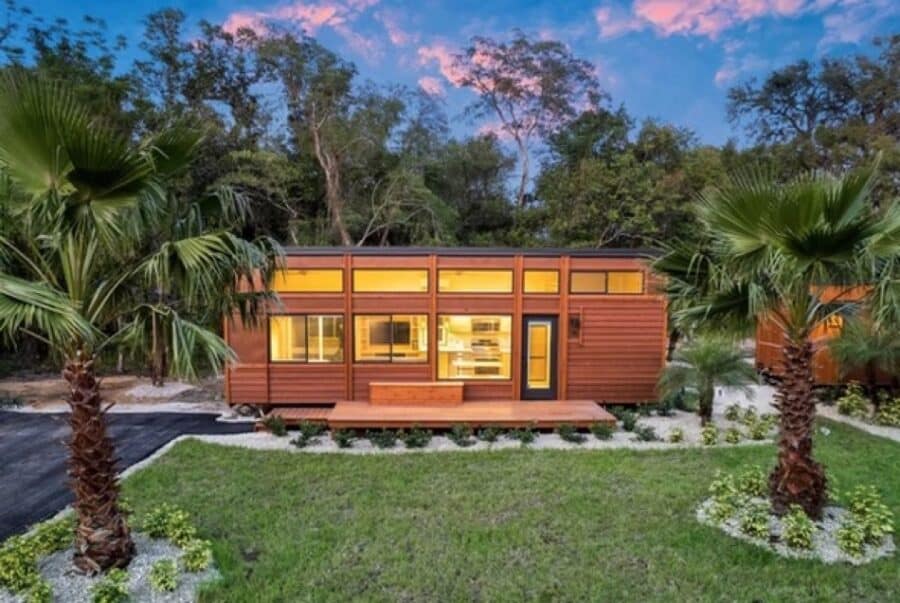 Tiny House with modern design and large windows in a lush, tropical setting.