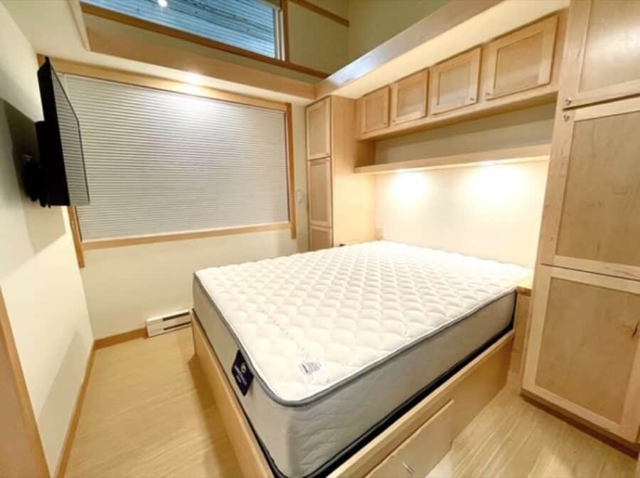 Compact tiny house bedroom with built-in wooden storage and a large window for natural light.