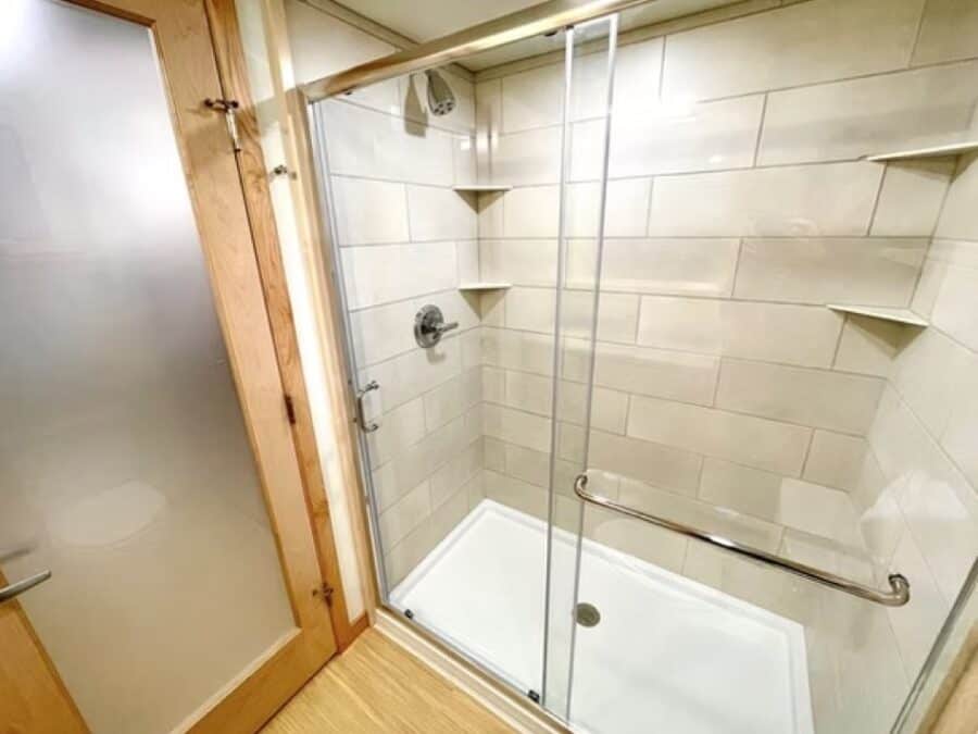 Compact tiny house shower with glass enclosure and built-in shelves.