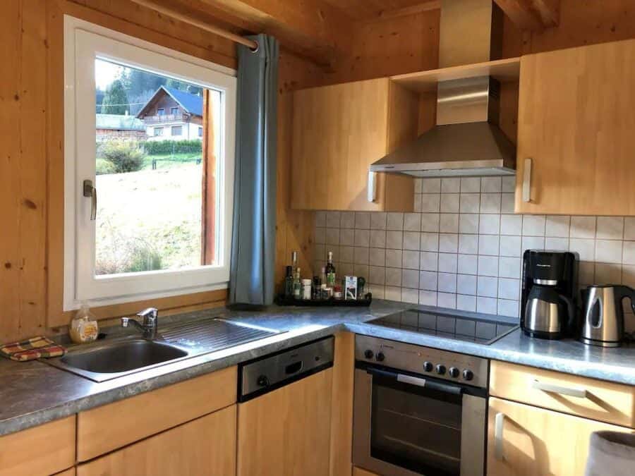 Small wooden chalet kitchen with modern appliances and a scenic view outside window.