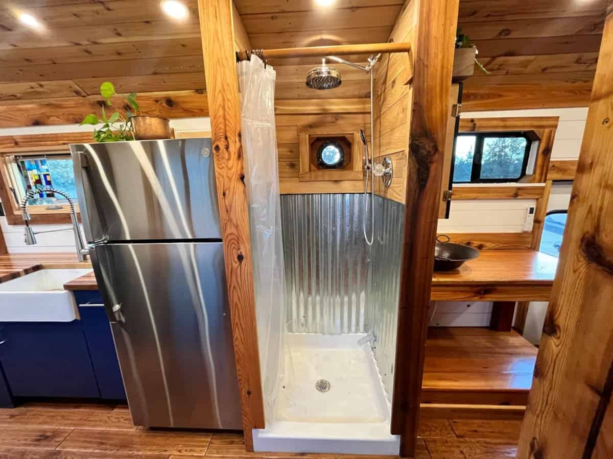 Corrugated metal shower with porthole window and wood framing in skoolie bathroom