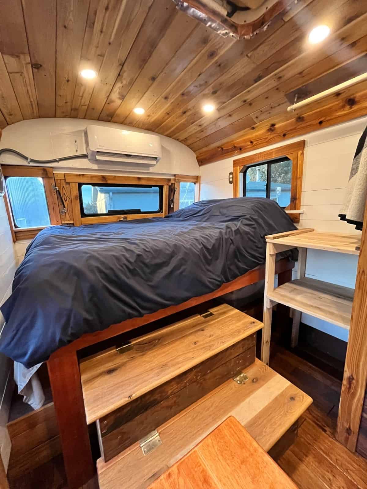 Raised platform bedroom with storage steps mini-split AC unit and wood ceiling
