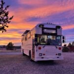 A white tiny house on wheels parked outdoors during a vibrant sunset.