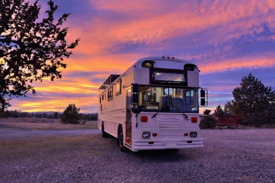 A white tiny house on wheels parked outdoors during a vibrant sunset.