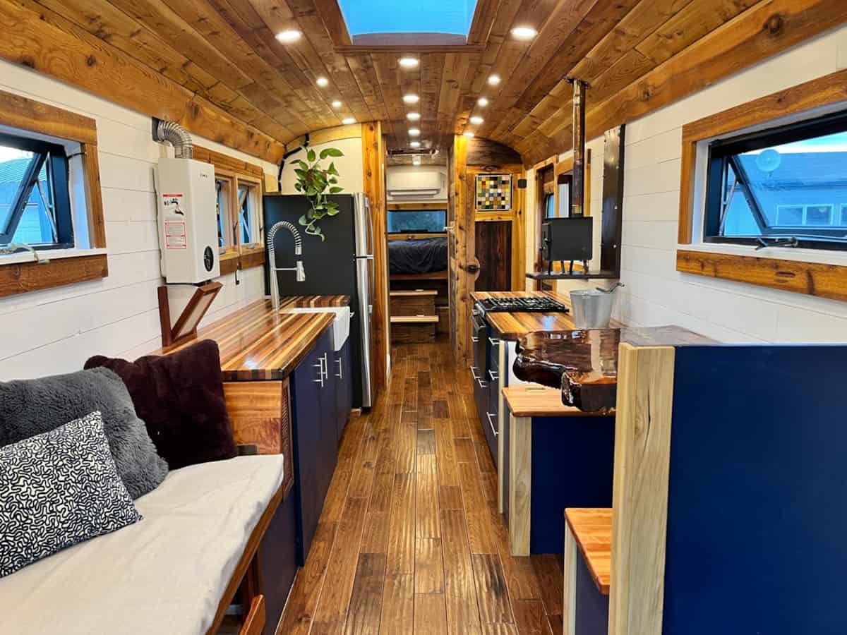 Full interior view of luxury skoolie showing kitchen living area and bedroom with hardwood floors and cedar ceiling