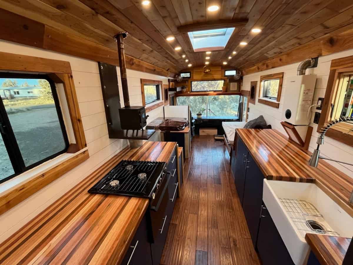 Galley kitchen with gas range farmhouse sink butcher block counters skylight and wood stove
