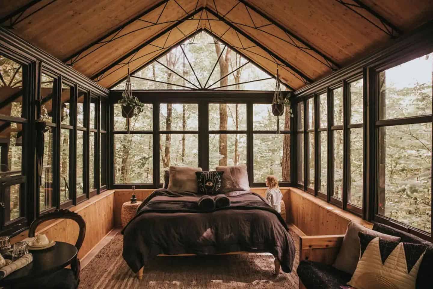 Tiny house treehouse bedroom with large windows and cozy decor.