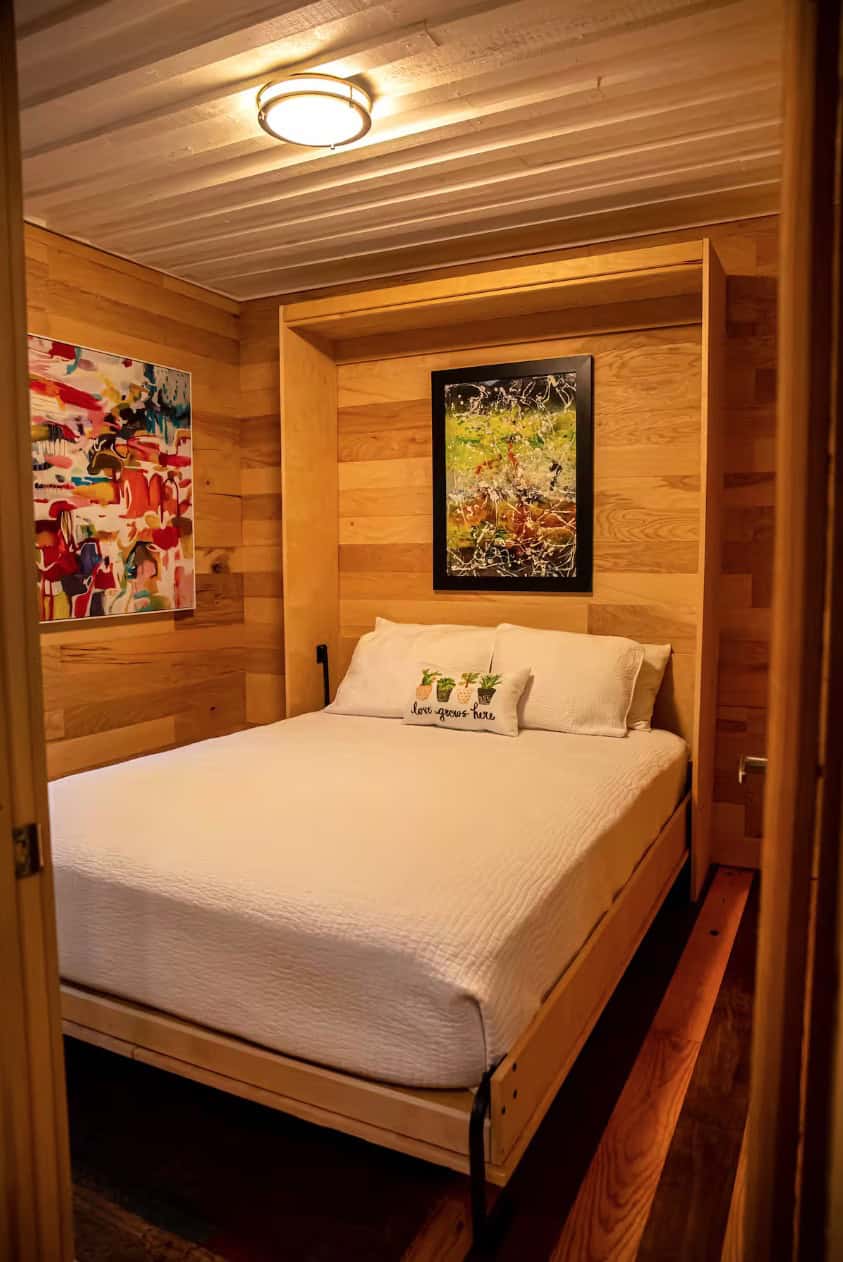 Compact tiny house bedroom with wooden interior and artwork.