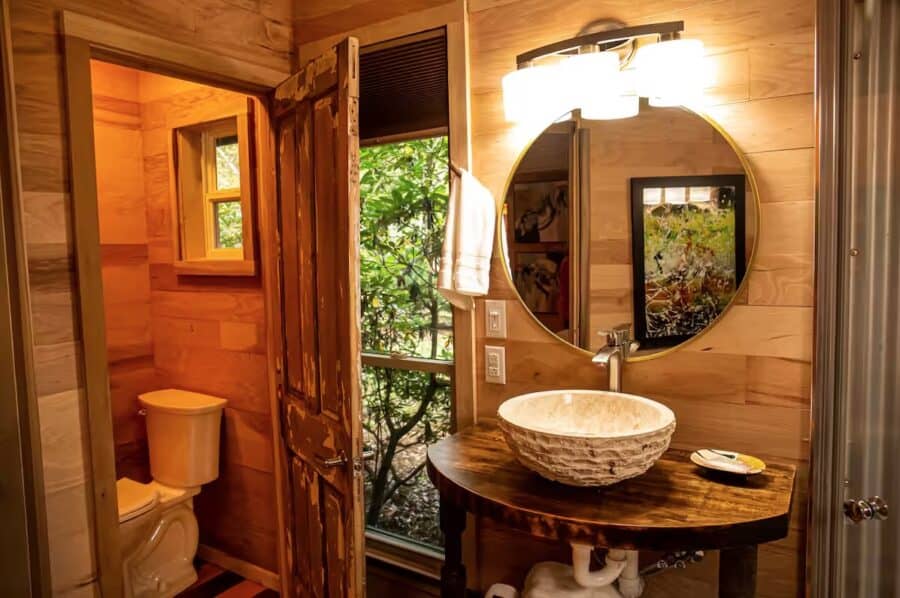 Charming tiny cabin bathroom with wooden accents and a view of lush greenery outside.