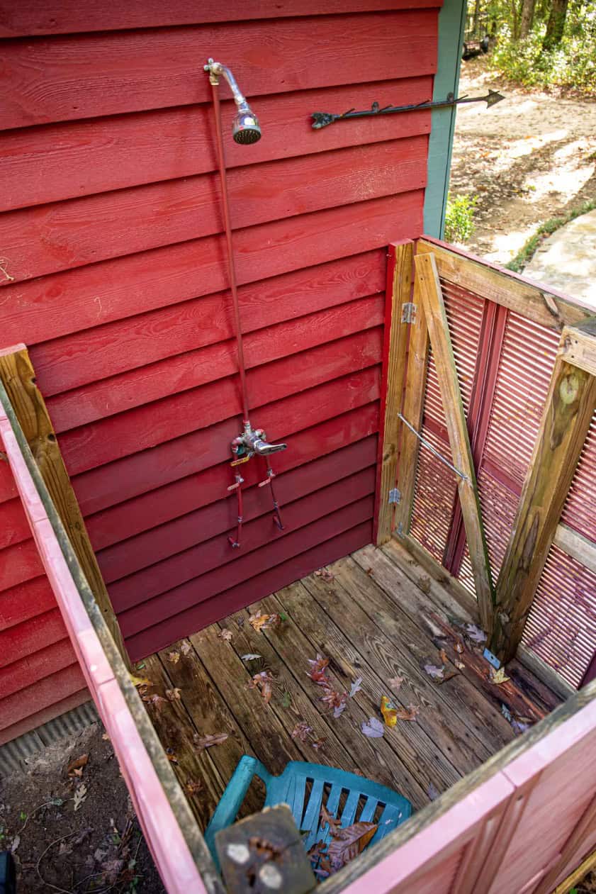 Outdoor shower on a rustic red cabin in the woods.