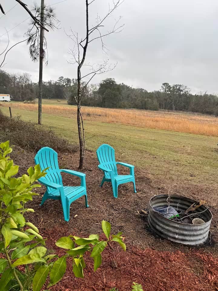Two teal Adirondack chairs and a galvanized fire pit overlooking an open pasture beside the Mantra cabin