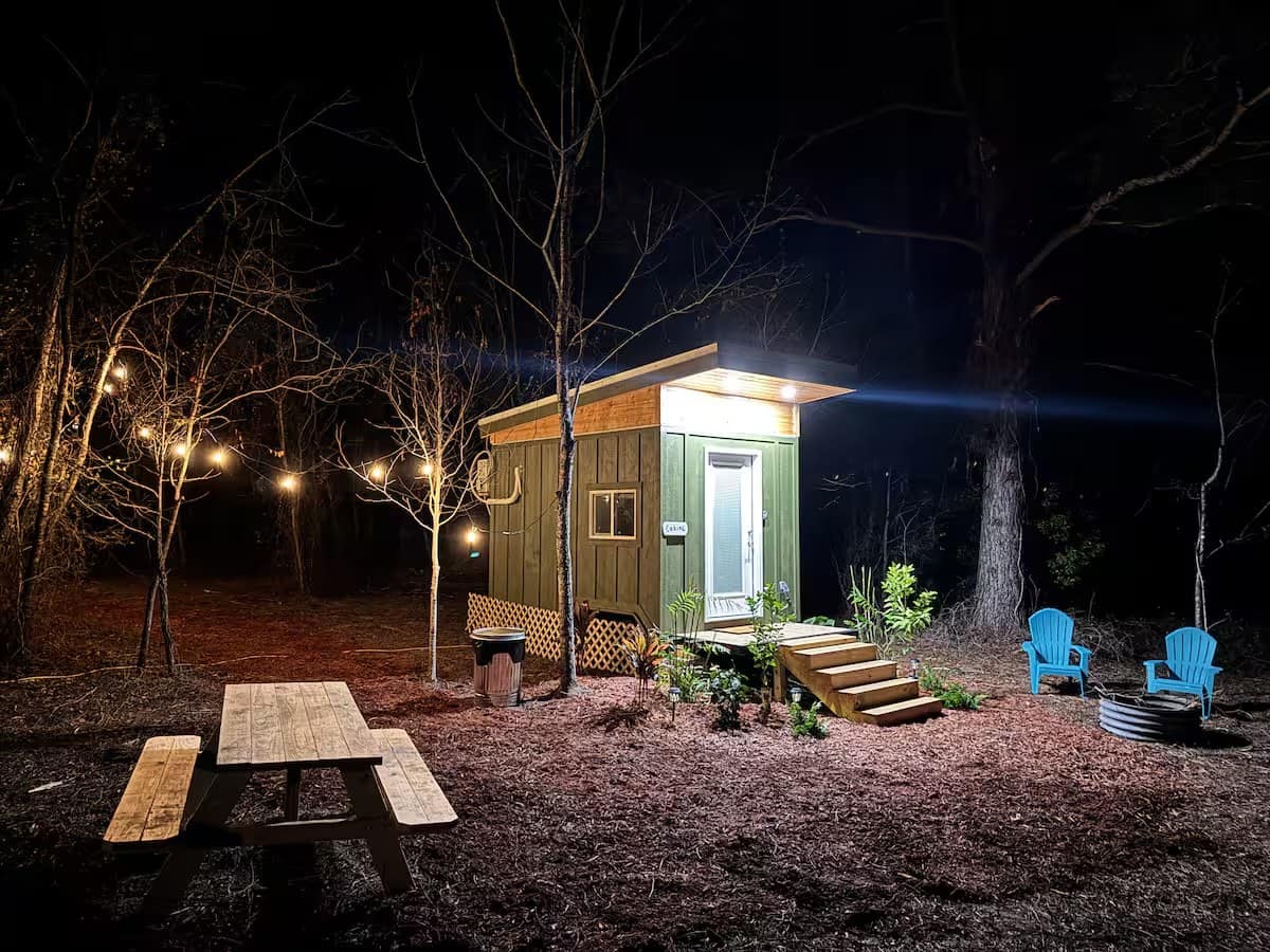The Mantra glamping cabin glowing at night with string lights, a picnic table, and a fire pit