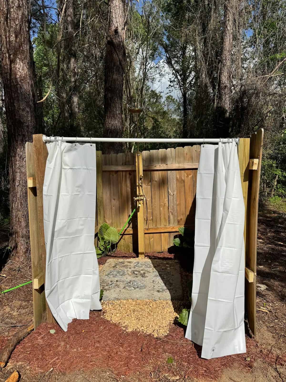 Outdoor shower enclosure with white privacy curtains and a stone floor in the North Florida woods
