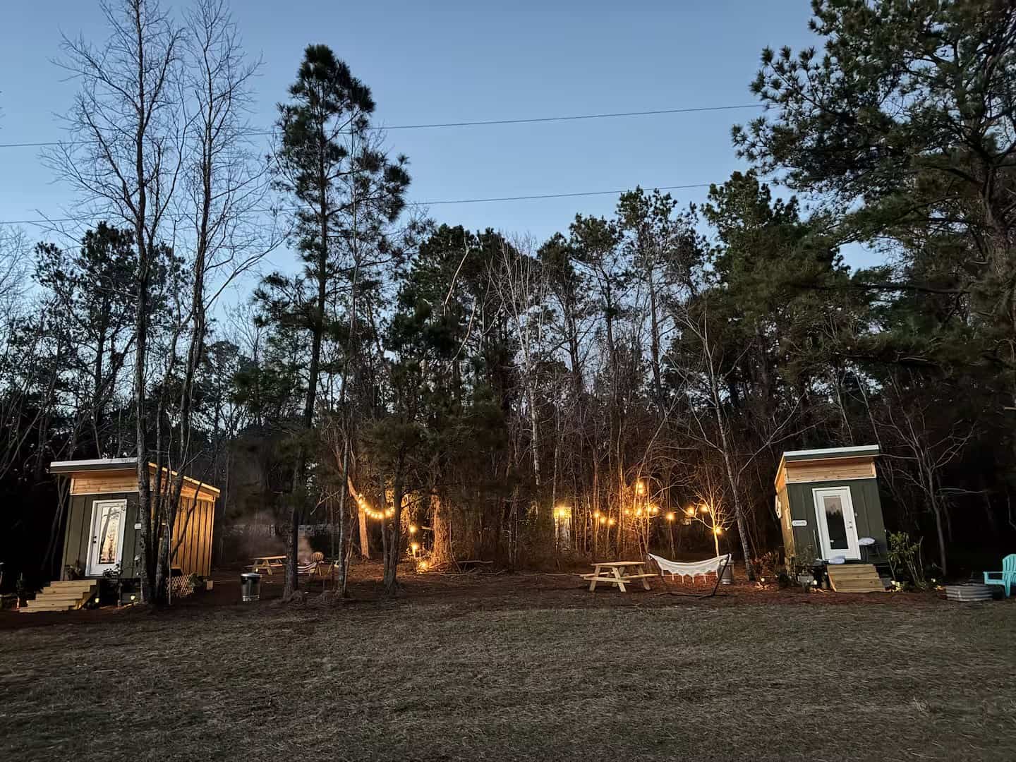 Two Mantra glamping cabins at dusk with string lights and a hammock strung between the trees