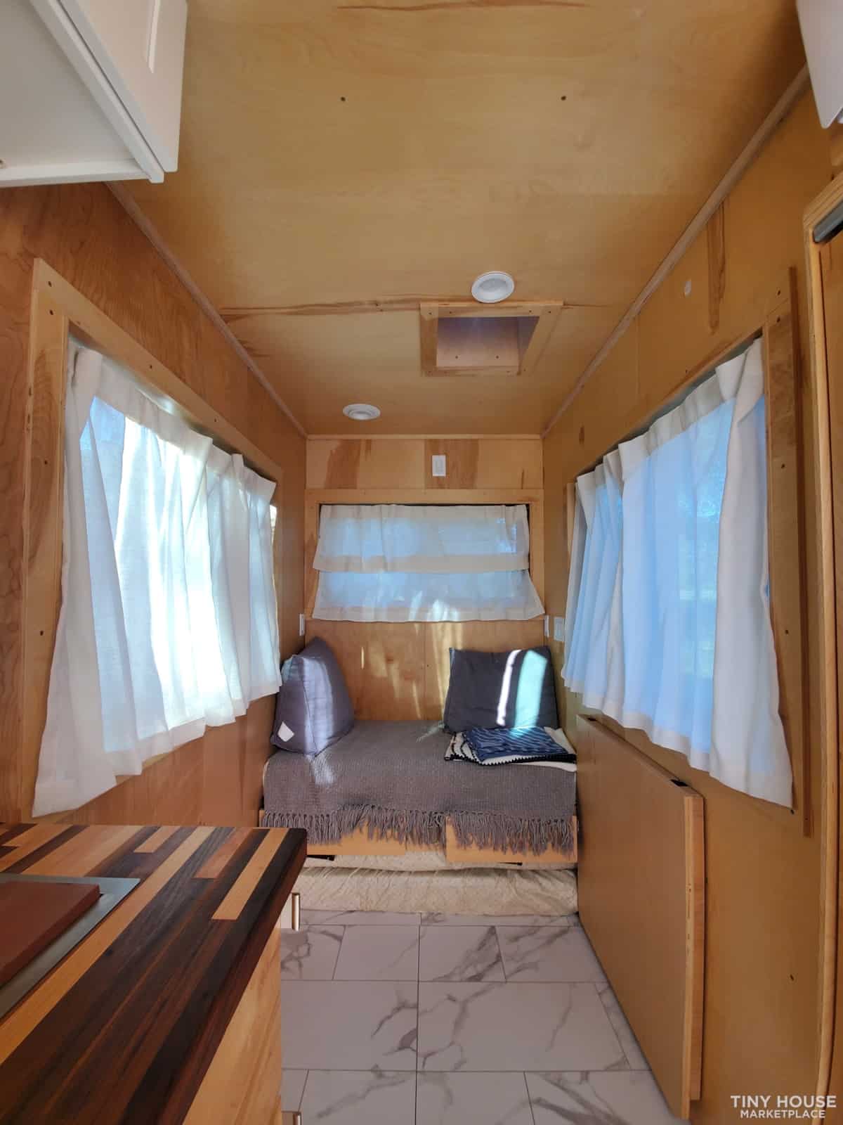 Small wooden tiny house interior with cozy seating and white curtains.
